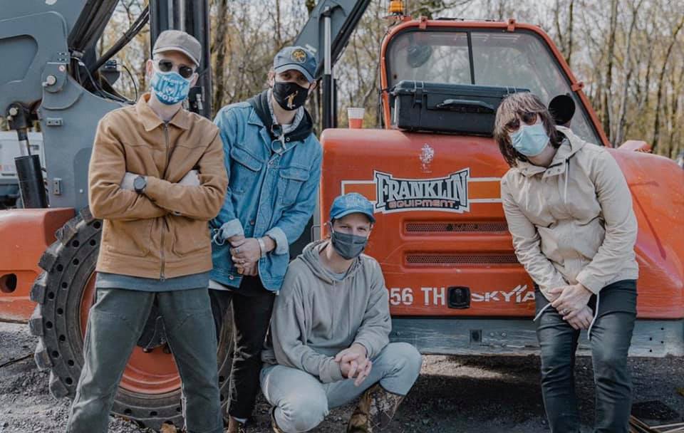 Colony House band members wearing masks posing in front of orange machinery