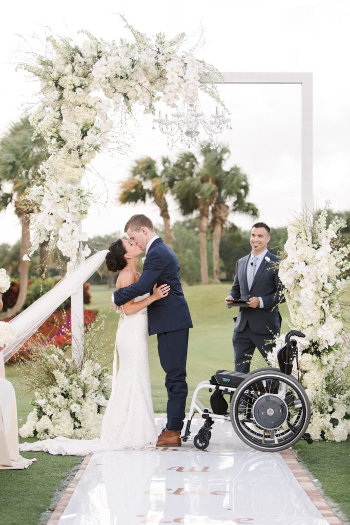 a wedding photo of chris standing out of his wheelchair kissing Emily at the altar